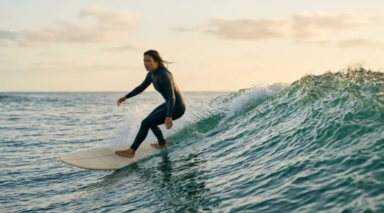 Intermediate surfer riding a clean green wave with focused stance and extended arms